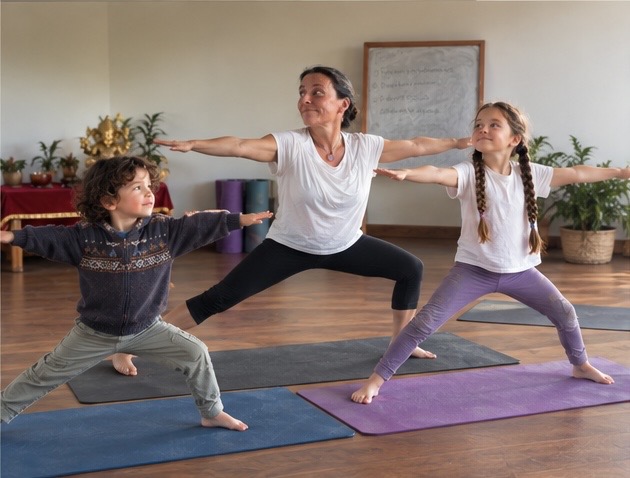 A parent and two children practising Warrior pose together on their yoga mats