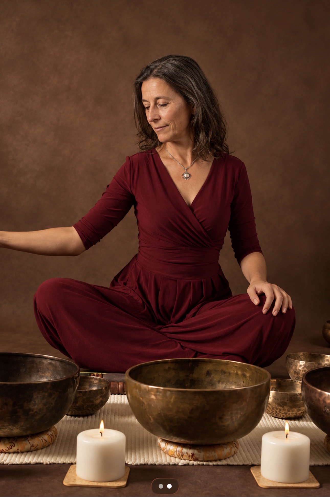 A woman sitting peacefully surrounded by Himalayan singing bowls and lit candles