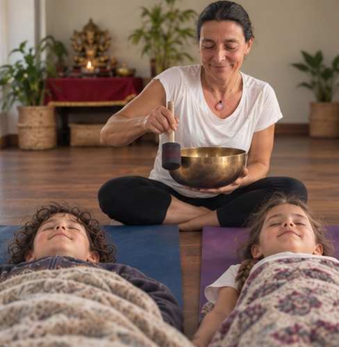 A parent playing a Himalayan singing bowl beside two resting children in relaxation